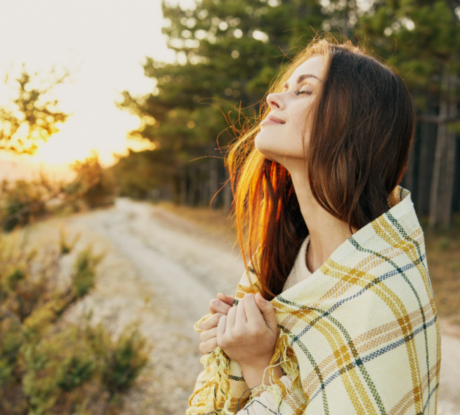 Frau steht mit einer Decke auf dem Weg und schaut in die Sonne